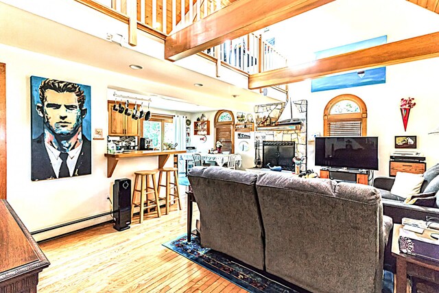 living room featuring baseboard heating, light wood-type flooring, and a high ceiling