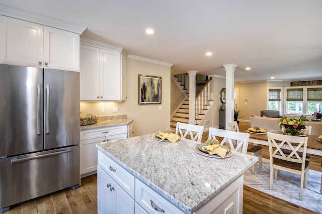 kitchen with ornate columns, white cabinetry, light stone counters, a kitchen island, and stainless steel refrigerator