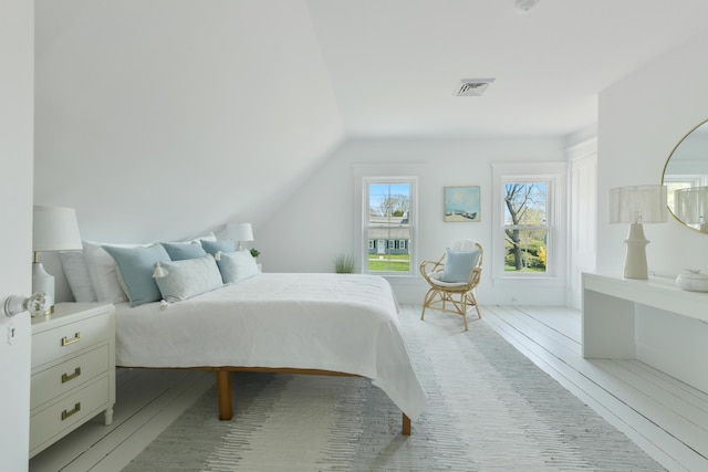 bedroom with visible vents, light wood-style flooring, and lofted ceiling