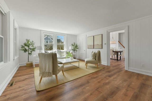 living area with baseboards, visible vents, wood finished floors, and a decorative wall