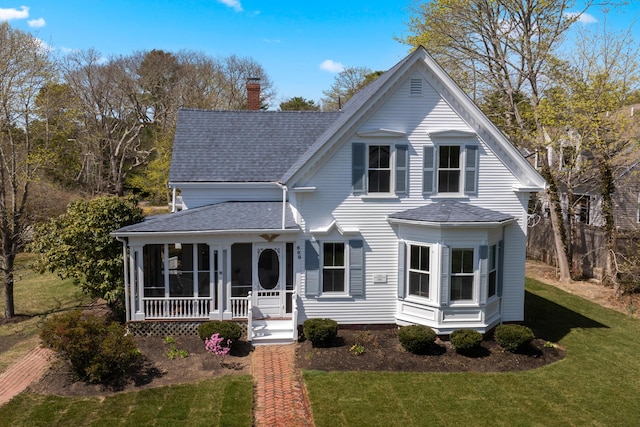 victorian-style house featuring a chimney, a porch, a front yard, and roof with shingles