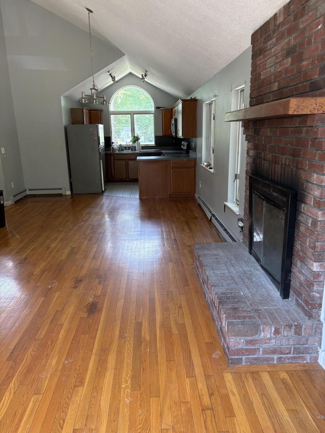 62 Musket Ln, Mashpee, MA 02649 - kitchen featuring stainless steel appliances, lofted ceiling, a baseboard radiator, a brick fireplace, and hardwood / wood-style flooring