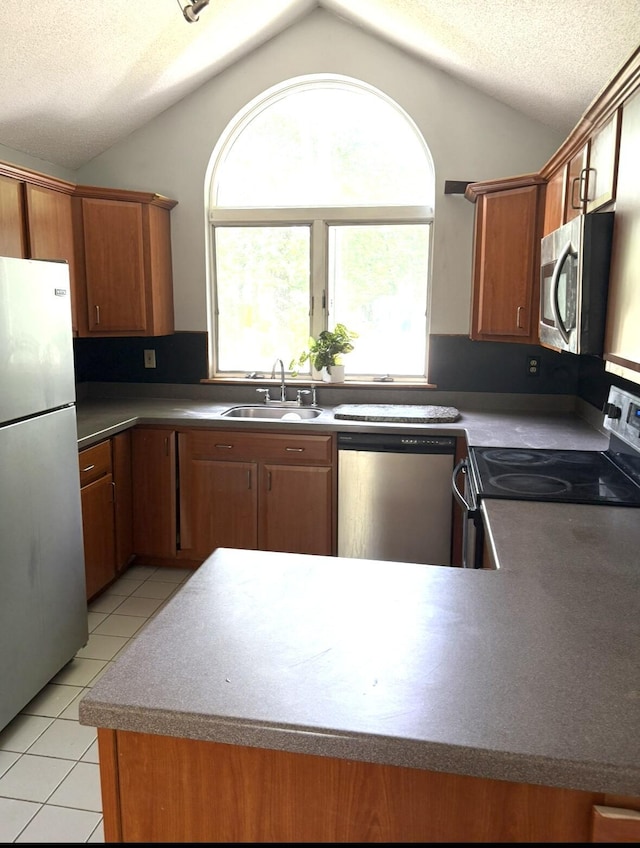 62 Musket Ln, Mashpee, MA 02649 - kitchen featuring appliances with stainless steel finishes, lofted ceiling, light tile patterned floors, brown cabinetry, and a textured ceiling