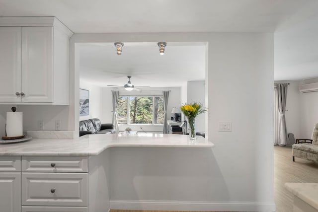 kitchen with a ceiling fan, white cabinetry, light countertops, and a wall unit AC