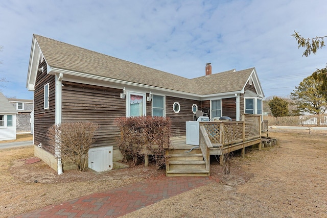 view of front facade featuring a deck, roof with shingles, and a chimney