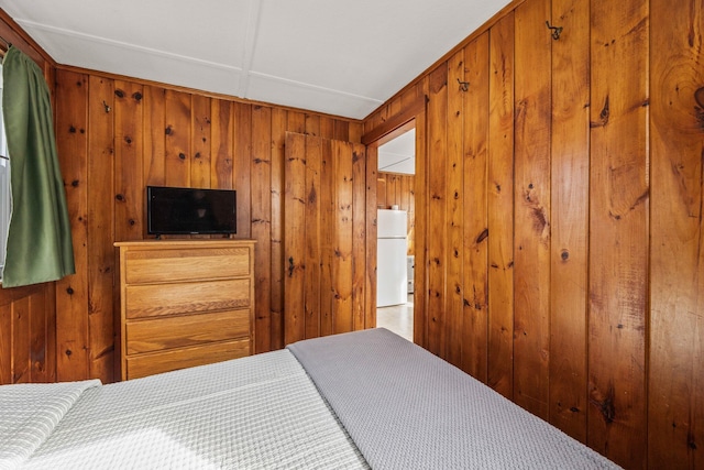 bedroom featuring wood walls and freestanding refrigerator