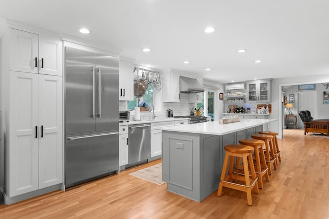 95 Red Brook Rd, Waquoit, MA 02536 - kitchen with appliances with stainless steel finishes, wall chimney range hood, light wood-style floors, light countertops, and a breakfast bar area