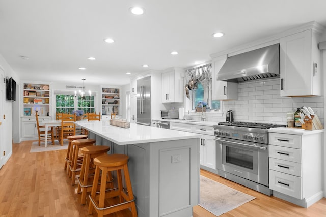 95 Red Brook Rd, Waquoit, MA 02536 - kitchen with wall chimney range hood, premium appliances, a center island, white cabinets, and a kitchen bar