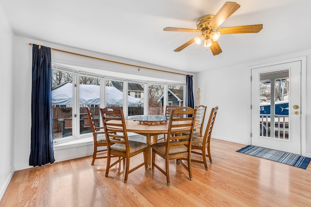 dining space featuring baseboards, a ceiling fan, and light wood finished floors