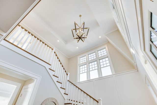 stairway with an inviting chandelier, a high ceiling, and a raised ceiling