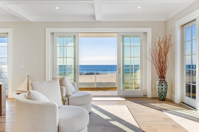 interior space with coffered ceiling, light wood-type flooring, a water view, a beach view, and beam ceiling