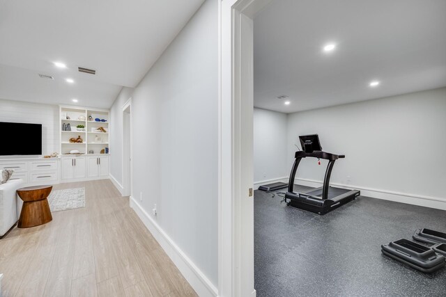 exercise room with light wood-type flooring and built in shelves