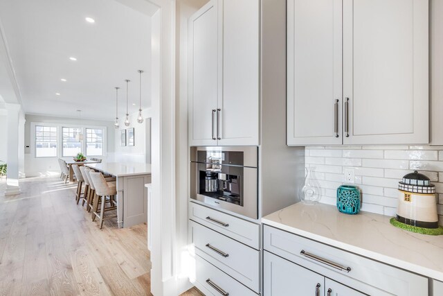 kitchen featuring light stone countertops, a kitchen bar, light hardwood / wood-style floors, hanging light fixtures, and oven