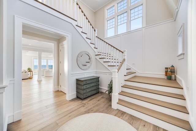 staircase featuring decorative columns, a high ceiling, crown molding, and hardwood / wood-style floors