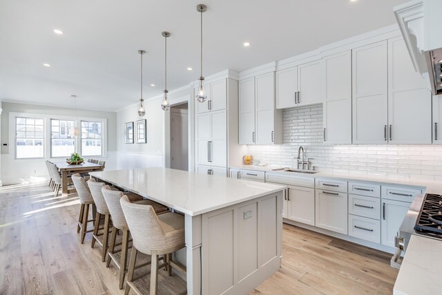 kitchen featuring a center island, sink, light wood-type flooring, white cabinets, and pendant lighting