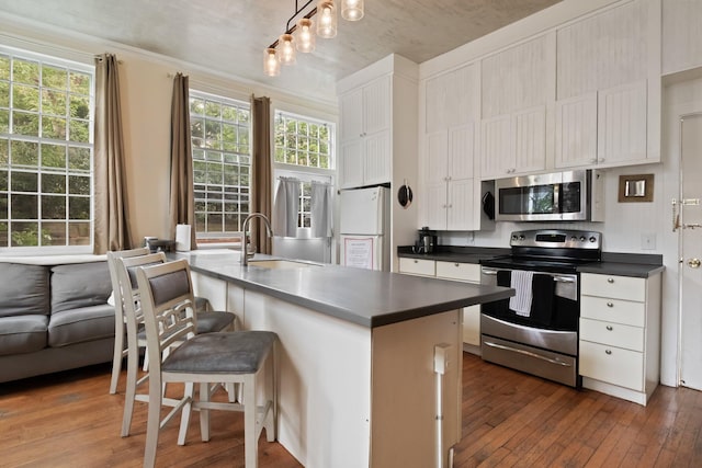 kitchen with appliances with stainless steel finishes, dark wood-type flooring, sink, a center island with sink, and a breakfast bar area