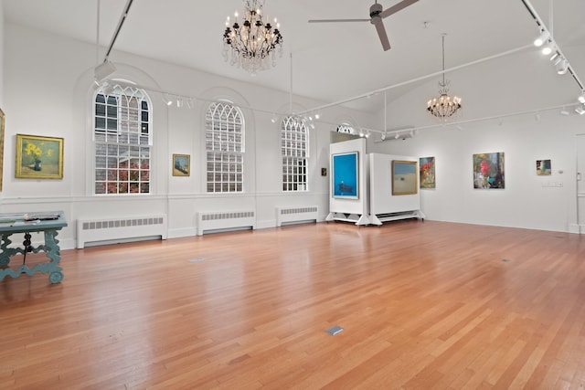 unfurnished living room with radiator heating unit, hardwood / wood-style floors, and ceiling fan with notable chandelier