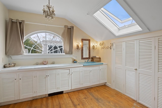 bathroom with wood-type flooring, an inviting chandelier, vanity, and lofted ceiling with skylight