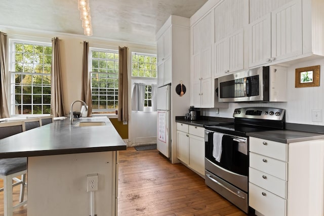 kitchen featuring white cabinets, stainless steel appliances, an island with sink, a kitchen breakfast bar, and hardwood / wood-style flooring