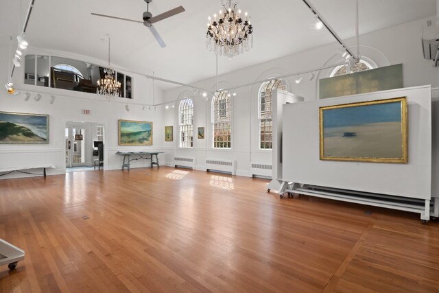 unfurnished living room featuring ceiling fan with notable chandelier, radiator, and wood-type flooring