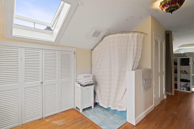 bedroom with vaulted ceiling with skylight and hardwood / wood-style floors