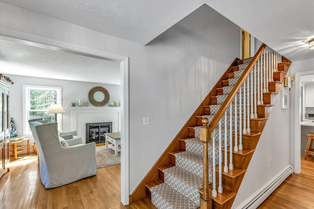 95 Red Brook Rd, Waquoit, MA 02536 - staircase featuring a baseboard radiator, wood finished floors, a brick fireplace, and a textured ceiling