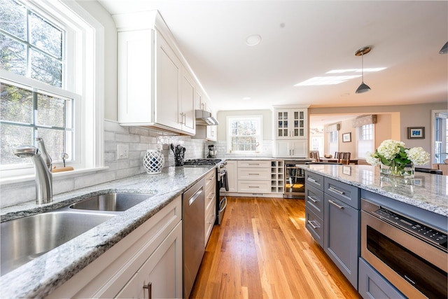 kitchen featuring a sink, stainless steel appliances, under cabinet range hood, white cabinetry, and backsplash