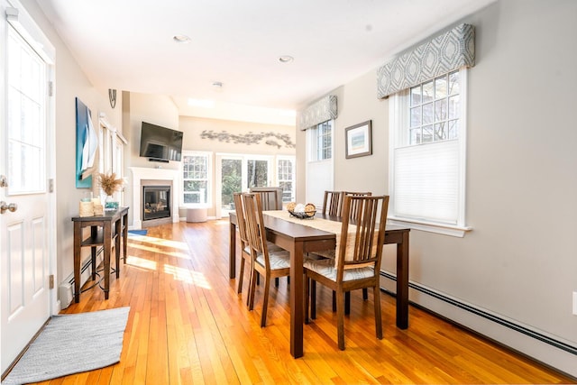 dining room with light wood finished floors, recessed lighting, baseboard heating, and a glass covered fireplace