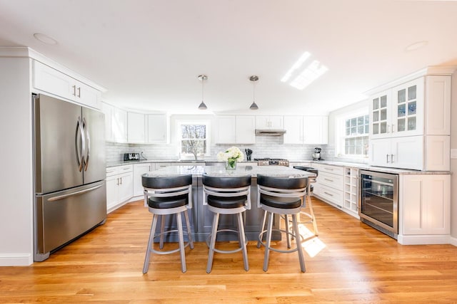 kitchen featuring beverage cooler, stainless steel fridge, plenty of natural light, and white cabinetry