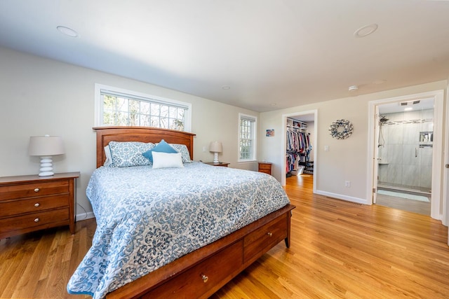 bedroom with a walk in closet, a closet, baseboards, and light wood finished floors