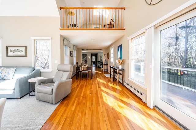 living room with a baseboard heating unit, light wood-type flooring, and a high ceiling