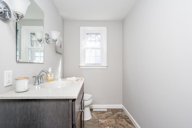 half bathroom featuring visible vents, baseboards, toilet, stone finish flooring, and vanity