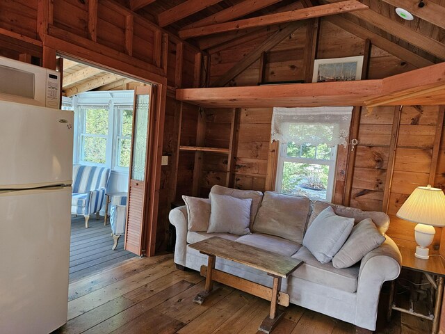 unfurnished living room featuring wood-type flooring, a healthy amount of sunlight, wood walls, and lofted ceiling