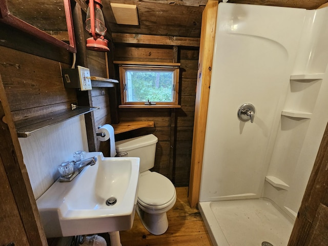 bathroom featuring toilet, a shower stall, a sink, wooden walls, and wood finished floors