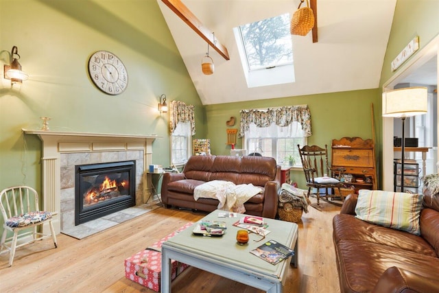 living room featuring a skylight, high vaulted ceiling, light hardwood / wood-style flooring, and a tiled fireplace