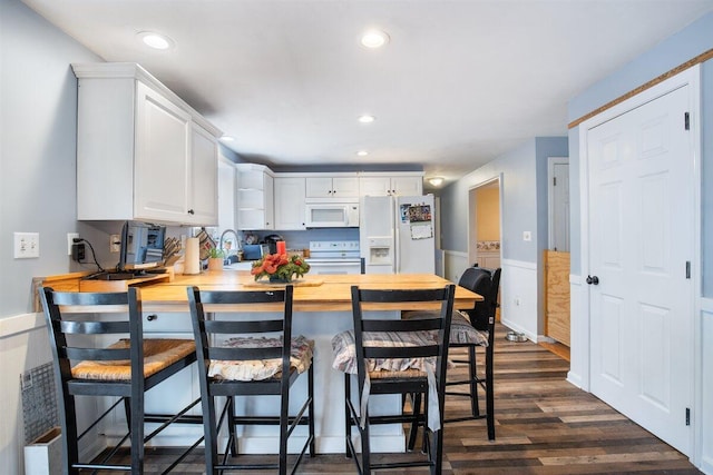 kitchen featuring white appliances, butcher block counters, white cabinets, dark hardwood / wood-style flooring, and a breakfast bar area