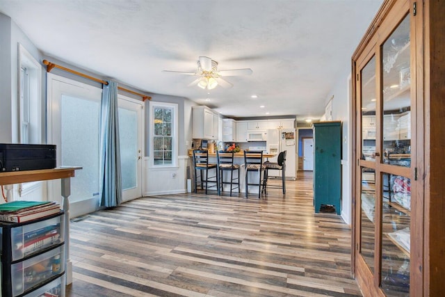 kitchen featuring ceiling fan, white cabinets, white appliances, light hardwood / wood-style floors, and a breakfast bar area