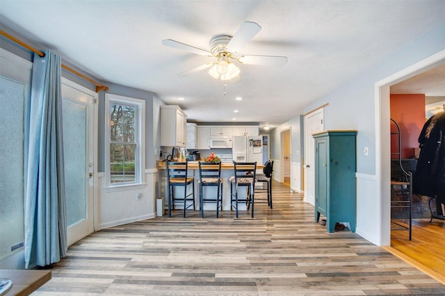 kitchen featuring ceiling fan, white cabinets, light wood-type flooring, white appliances, and a kitchen bar