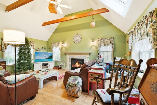 living room with ceiling fan, a skylight, beam ceiling, and light wood-type flooring