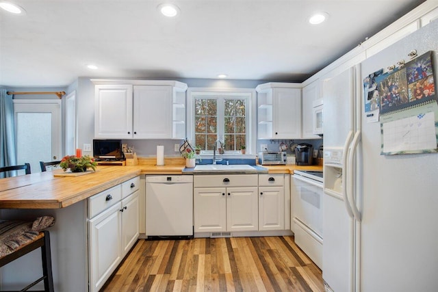 kitchen featuring white appliances, butcher block counters, white cabinets, kitchen peninsula, and a breakfast bar area