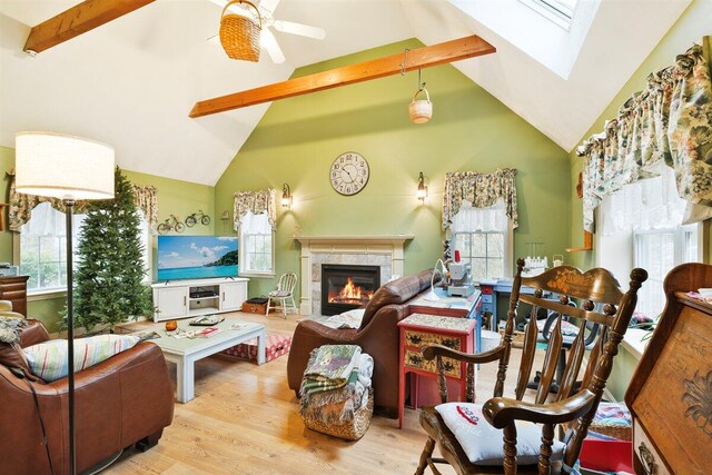 living room featuring light hardwood / wood-style floors, ceiling fan, a skylight, and beamed ceiling