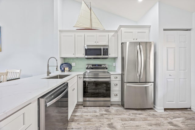 kitchen with hanging light fixtures, sink, white cabinets, stainless steel appliances, and lofted ceiling