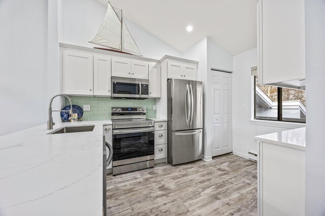 kitchen with appliances with stainless steel finishes, sink, white cabinets, decorative backsplash, and lofted ceiling