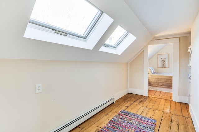 additional living space featuring a baseboard heating unit, wood-type flooring, and vaulted ceiling with skylight