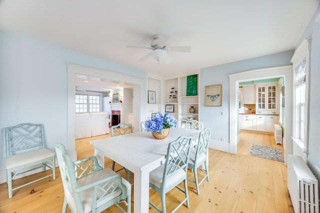 dining room featuring ceiling fan, a fireplace, radiator, and light hardwood / wood-style flooring