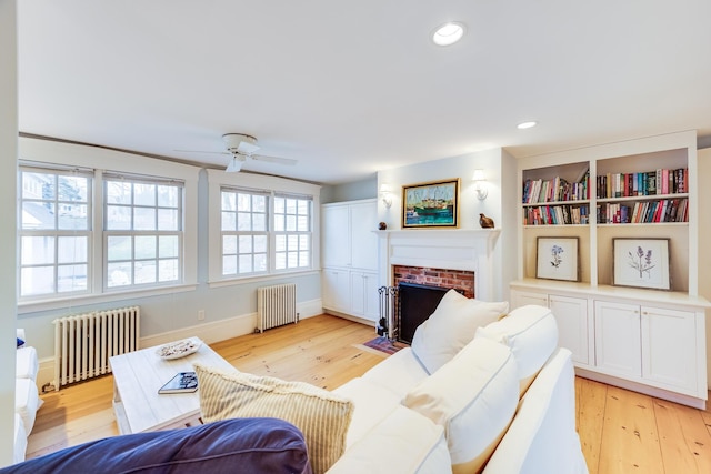 living room featuring a brick fireplace, radiator heating unit, and light hardwood / wood-style floors