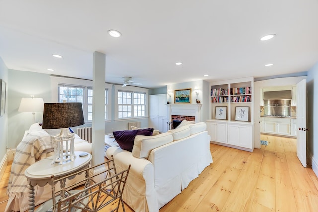 living room featuring ceiling fan, a fireplace, and light wood-type flooring