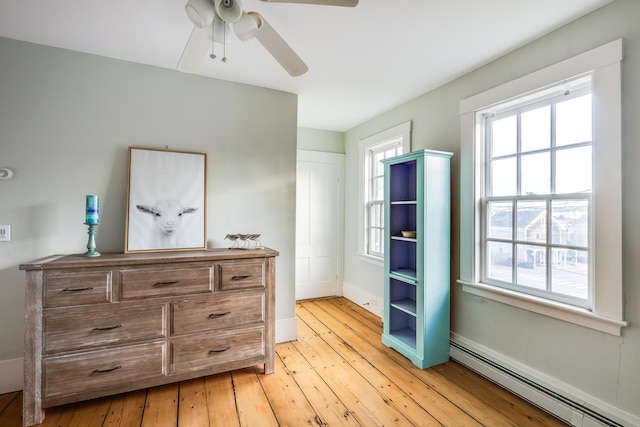 bedroom featuring ceiling fan, light wood-type flooring, and a baseboard heating unit