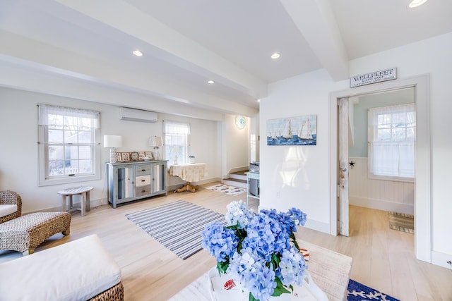 living room with beam ceiling, a wall mounted AC, and light wood-type flooring