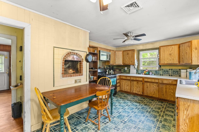 kitchen featuring black gas stove, a ceiling fan, light countertops, stainless steel microwave, and dark flooring